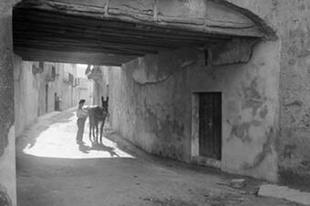 Un home i el seu ase s'aturen sota una volta, cap al 1930.